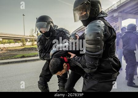 Erfahrene Bereitschaftspolizei in Helmen hält die Hände des Rebellen hinter seinem Rücken, während sie Menschen bei einer Kundgebung festhält Stockfoto