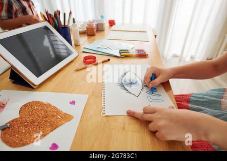 Kleines Mädchen, das Bilder mit Filzstiften am Tisch im Spielzimmer zeichnet Stockfoto