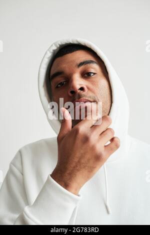 Vertikales Porträt eines robusten lateinamerikanischen Mannes mit weißem Hoodie und Blick auf die Kamera Stockfoto