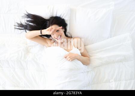 Lächelnde junge Frau, die morgens nach einem guten Schlaf in einem komfortablen weißen Bett aufwachte Stockfoto