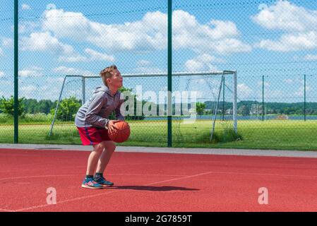 Junge Vorbereitung für Basketball-Schießen auf Playground.Boy führt Schuss bei Basketball-Spiel auf dem Spielplatz während sonnigen Sommertag. Stockfoto