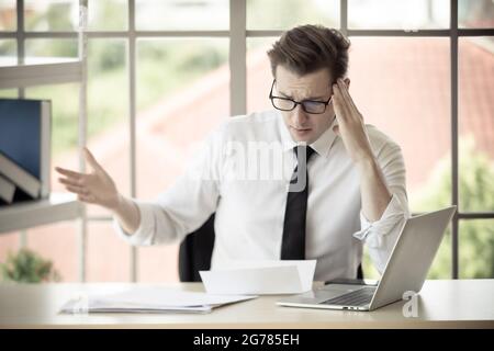 Der junge kaukasische Geschäftsmann, der eine Brille trägt, ist schockiert und ängstlich, wenn er den Brief liest, in dem er von seiner Arbeit im Büro entlassen wird. Konzept für Mitarbeiter une Stockfoto