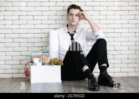 Junge kaukasische Geschäftsmann müde sitzen mit fühlen sich traurig, gestresst, hoffnungslos und unglücklich Gesicht neben Box mit Habseligkeiten aus dem Büro am Ende gesammelt Stockfoto