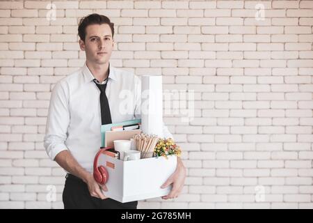 Junger kaukasischer Geschäftsmann in legerem Hemd mit einem traurigen, gestressten und unglücklichen Gesicht, das einen Papierkarton mit Habseligkeiten hält, die im Büro gesammelt wurden Stockfoto