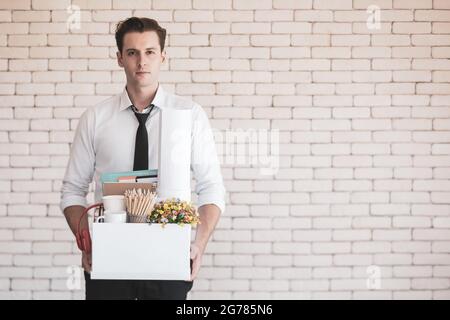 Junger kaukasischer Geschäftsmann in legerem Hemd mit einem traurigen, gestressten und unglücklichen Gesicht, das einen Papierkarton mit Habseligkeiten hält, die im Büro gesammelt wurden Stockfoto