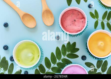 Kohlenhydratarme Eiscreme. Sommerliche Lebensmittelkomposition mit verschiedenen hausgemachten, veganen, Fruchteis, Blättern, Heidelbeeren und Holzlöffeln auf blauem Hintergrund Stockfoto