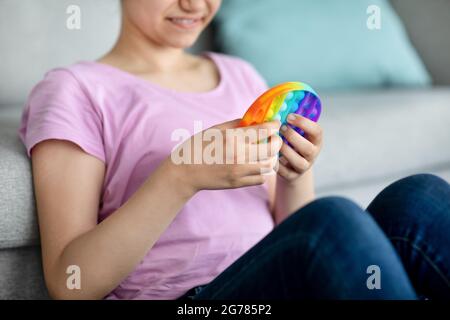 Beschnittene Ansicht eines indischen Teenagers, das zu Hause mit Anti-Stress-POP-IT-Spielzeug spielt, Nahaufnahme der Hände Stockfoto