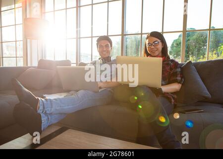 Verschiedene Paar Liebhaber, kaukasischen Mann und asiatische Frau sitzen auf dem Sofa im Wohnzimmer und halten Laptop Notebook-Computer zu Hause arbeiten zusammen in t Stockfoto