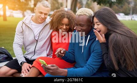 Multi ethnische Freunde im Freien suchen Smartphone-Bildschirm. Diverse Gruppe Menschen Afro american asiatisch kaukasisch verbringen Zeit zusammen multirassischen männlichen Fem Stockfoto