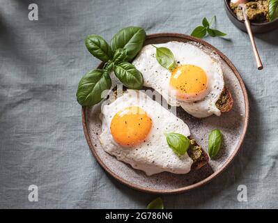 Croque-madame mit Spiegelei, Pesto-Sauce und Basilikum auf einem Leinentischtuch. Traditionelles Französisches Geröstetes Sandwich. Französische Küche. Speicherplatz kopieren, selektiv Stockfoto