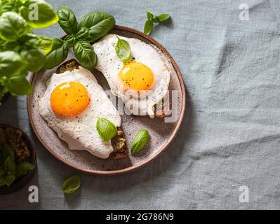 Croque-madame mit Spiegelei, Pesto-Sauce und Basilikum auf einem Leinentischtuch. Traditionelles Französisches Geröstetes Sandwich. Französische Küche. Speicherplatz kopieren, selektiv Stockfoto