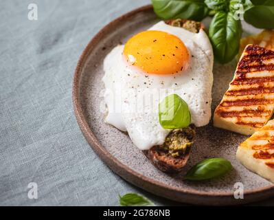 Croque-madame mit Spiegelei, Pesto-Sauce und Basilikum auf einem Leinentischtuch. Traditionelles Französisches Geröstetes Sandwich. Französische Küche. Speicherplatz kopieren, selektiv Stockfoto