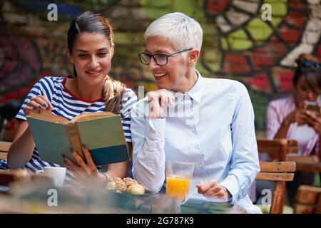 Junge Erwachsene Frau, die zusammen mit älteren kaukasischen Frauen ein Buch liest. Stockfoto