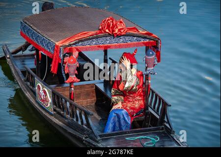 Wuxi, China - Oktober 2019: Frau in traditioneller chinesischer Hochzeitskleidung auf einem geschmückten Flussschiff, vor blauem Hintergrund. Stockfoto