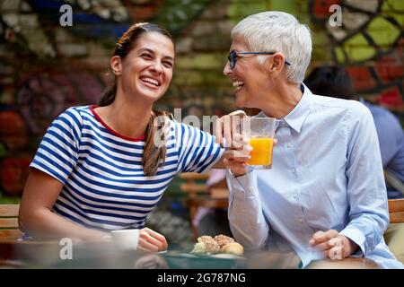 Weibliche Freunde oder Erwachsene Tochter und Mutter Konzept. Junge Frau lachen laut mit älteren kaukasischen Frau, sitzen im Café im Freien. Stockfoto