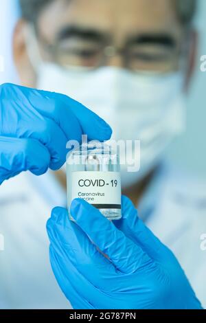 Hand eines Arztes oder Forschers, der eine schützende Hygienemaske in medizinischen blauen Handschuhen trägt und auf eine Flasche COVID-19-Coronavirus-Impfstoff zeigt. Stockfoto