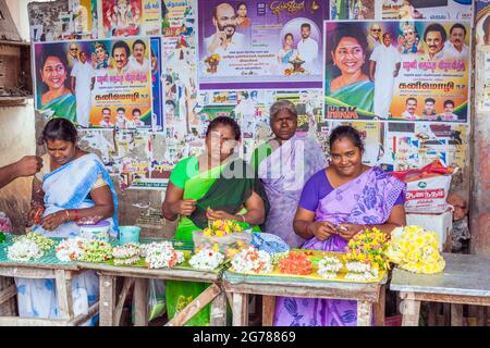 Indische Weibchen am Marktstand, die Blumengirlanden als Puuja-Tempelopfer vor bunten Plakaten verkaufen, Tamil Nadu, Indien Stockfoto