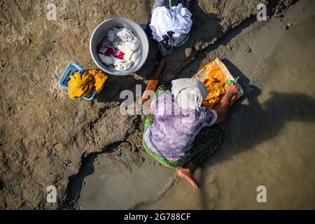 Frau, die an einem Flussufer in Sagaing, Myanmar, ihre Kleidung von Hand waschen muss. Luftaufnahme einer Frau mit Turban, die am Ufer des Irrawadden River Wäsche waschen soll Stockfoto