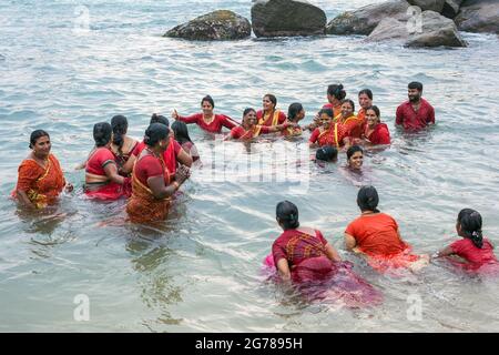 Gruppe von hinduistischen weiblichen Anbetern, die rote Saris tragen und im Ozean baden, Kanyakumari, Laccadive Sea, Tamil Nadu, Indien Stockfoto