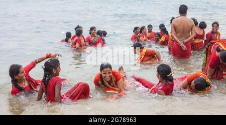 Gruppe von hinduistischen weiblichen Anbetern, die rote Saris tragen und im Ozean baden, Kanyakumari, Laccadive Sea, Tamil Nadu, Indien Stockfoto