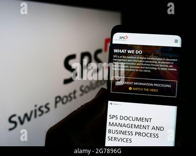 Person, die Telefon mit der Webseite der Dokumentenmanagementfirma Swiss Post Solutions (SPS) auf dem Bildschirm mit Logo hält. Konzentrieren Sie sich auf die Mitte des Telefondisplays. Stockfoto