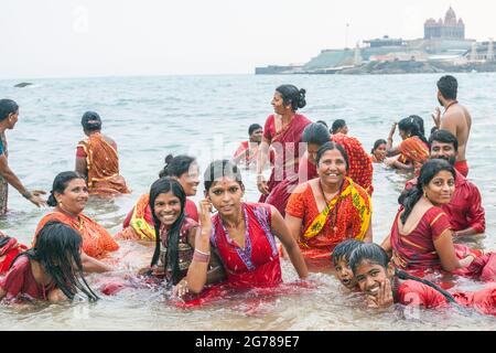 Eine Gruppe von hinduistischen weiblichen Anbetern in roter Kleidung baden vor dem Vivekanand Rock Memorial, Kanyakumari, Laccadive Sea, Tamil Nadu, Indien Stockfoto