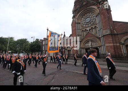 Orangemen marschieren im Rahmen der Feierlichkeiten vom 12. Juli, die den Sieg von König Wilhelm von Oranien über den katholischen König James bei der Schlacht an der Boyne im Jahr 1690 feiern, an der katholischen Kirche St. Patrick in Belfast vorbei. Stockfoto