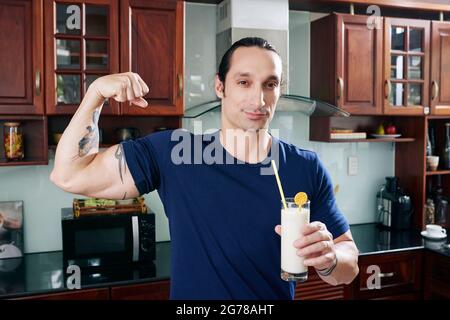 Porträt von fröhlich fit Mann hält Protein-Banane-Cocktail und Biegen Bizeps Muskeln Stockfoto