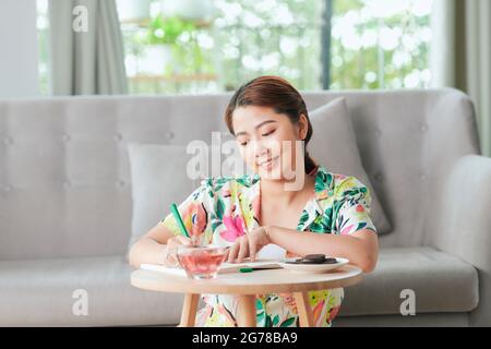 Entspannte Frau, die im Wohnzimmer auf dem Boden sitzt und Tagebuch schreibt Stockfoto