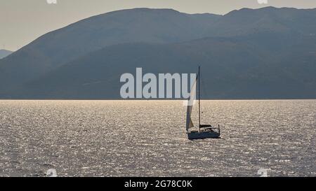 Ionische Inseln, Ithaca, Insel Odysseus, Überquerung zwischen Poros auf Kefaloniia und dem Hafen von Aetos auf Ithaca, Segelboot vor Ithaca im Hintergrund, Glitzer auf dem Wasser, Segel wehend, im Hintergrund die Bergketten von Kefalonia Stockfoto