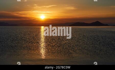 Ionische Inseln, Ithaca, Insel Odysseus, Frikes, Sonnenaufgang, Morgenlicht, Morgenstimmung, Sonne geht über dem Festland auf, Sonnenstrahl auf dem Meer, himmelblau bis orange, leichte Wolkendecke Stockfoto