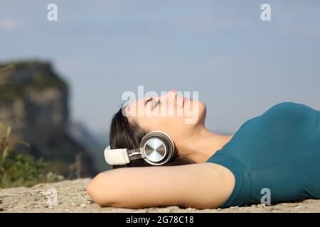 Seitenansicht Porträt einer asiatischen Frau, die in der Natur lügt und Musik hört Stockfoto