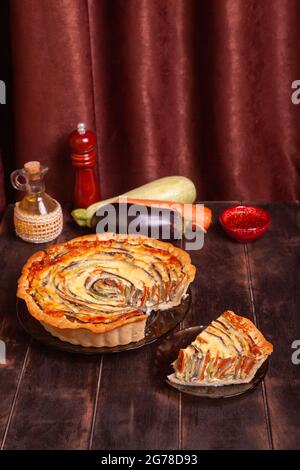 Das geschnittene Stück Gemüsespiraltorte mit Zucchini, Auberginen, Karotte auf Holzhintergrund. Stockfoto