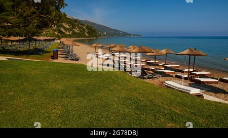 Ionische Inseln, Zakynthos, südlich der Stadt Zakynthos, Banana Beach, grüner Rasen, hinter Sonnenschirmen und Sonnenliegen, keine Menschen, blaues Wasser, blauer Himmel Stockfoto