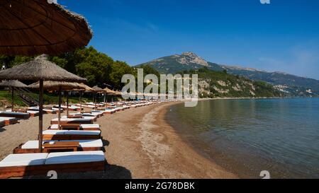 Ionische Inseln, Zakynthos, südlich der Stadt Zakynthos, Banana Beach, halbrunde Bucht, Sandstrand, aufgereihte Sonnenliegen mit Sonnenschirmen, Meer grün-blau, himmelblau, Berg im Hintergrund Stockfoto