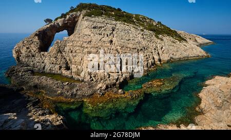 Ionische Inseln, Zakynthos, Westküste, Adria, Korakonissi, Weitwinkelansicht der ganzen Insel, scheint auf dem kristallklaren Wasser zu schweben, Inselchen wuchsen auf der Rückseite, die Insel hat ein Loch auf der linken Seite (Felsentor), das Wasser ist grün-blau, der Himmel ist tiefblau und wolkenlos Stockfoto