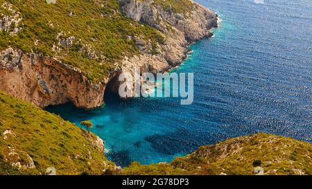 Ionische Inseln, Zakynthos, Westküste, Adria, Strand, Hafen, Porto Vromi, Blick hinunter in die Bucht, überwucherter Hügel und einzelner Baum im Vordergrund, türkisfarbenes Meer in der Mitte, felsige Küste mit Einbuchtung auf der anderen Seite der Bucht, kein Himmel Stockfoto