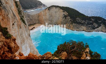 Zakynthos, Paralia Navagio, Shipwreck Beach, Blick von oben über die gesamte Bucht und einen Teil des Strandes, Schiffswrack MV Panagiotis, schweres Meer, Wellen Rollen auf den Strand, rauschendes Wasser, türkisfarbenes Wasser, Felsen im Vordergrund Stockfoto