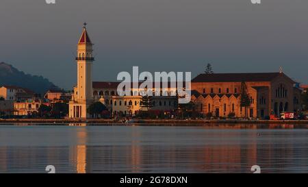 Zakynthos, Zakynthos Stadt, Morgenlicht, Blick über den Hafen auf die Kirche von Agios Dionysios und ihren Glockenturm. Der Turm spiegelt sich zum Teil im stillen Wasser. Im Bild rechts das Hauptschiff der Kirche. Stockfoto