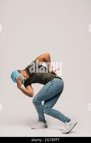 Unerkannte lateinische Tänzerin mit Hut und Spaß im Studio vor weißem Hintergrund mit Hip-Hop-Moves. Stockfoto