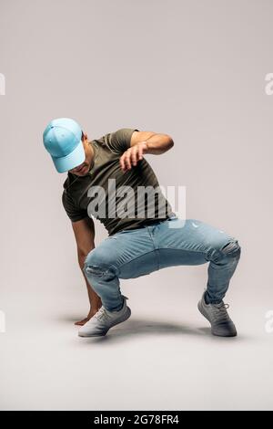 Unerkannte lateinische Tänzerin mit Hut und Spaß im Studio vor weißem Hintergrund mit Hip-Hop-Moves. Stockfoto