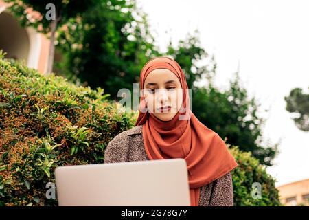 Schöne junge Frau trägt Kopftuch im Park sitzen und mit ihrem Computer. Stockfoto