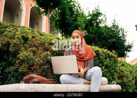 Schöne junge Frau trägt Kopftuch im Park sitzen und mit ihrem Computer. Stockfoto