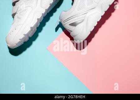 Draufsicht weiße Sneakers auf der Seite auf einem zarten geometrischen Papier rosa und blauen Hintergrund mit harten Schatten, Kopierraum für Text, Morgen Stockfoto