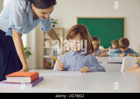 Die Grundschülerin in der Klasse macht mit Hilfe einer Lehrerin einen Schulauftrag. Stockfoto