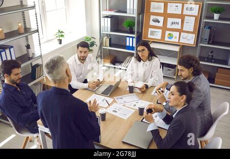 Die Mitarbeiter hören den Führungskräften zu, die in der Unternehmensbesprechung am Bürotisch sitzen Stockfoto