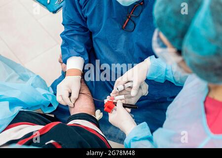 Ein nicht anerkannter Arzt, der Latexhandschuhe trägt, entzieht einem Patienten in der medizinischen Klinik Blut. Stockfoto