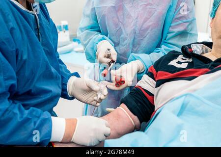 Ein nicht anerkannter Arzt, der Latexhandschuhe trägt, entzieht einem Patienten in der medizinischen Klinik Blut. Stockfoto