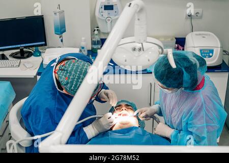 Zahnarzt-Team trägt Gesichtsmasken und Haarnetze arbeiten in der Zahnklinik mit erwachsenen Patienten. Stockfoto