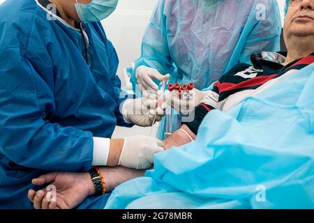 Ein nicht anerkannter Arzt, der Latexhandschuhe trägt, entzieht einem Patienten in der medizinischen Klinik Blut. Stockfoto